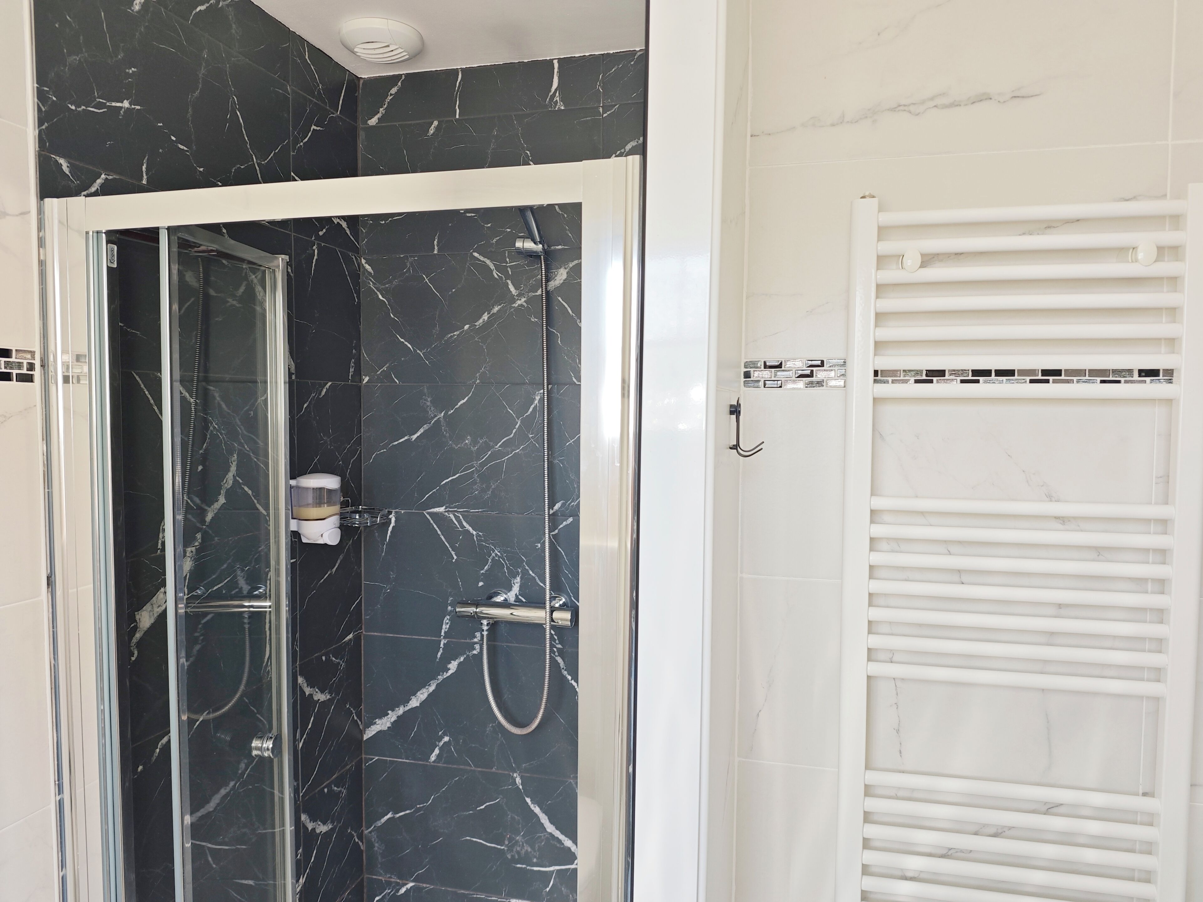 A bathroom with a glass-enclosed shower, a white towel rack, and a tiled wall with a marble pattern.