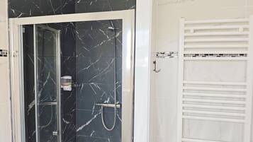 A bathroom with a glass-enclosed shower, a white towel rack, and a tiled wall with a marble pattern.