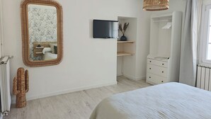 Un dormitorio con una cama grande, un espejo, un televisor, un armario y una lámpara colgante.