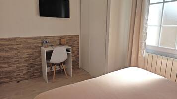 A hotel room with a bed, a desk with a chair, a television mounted on the wall, and a window with curtains.