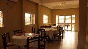 A dining area with multiple tables and chairs, large windows, and a view of the outside. - Hotel Massoh (Bertoua)