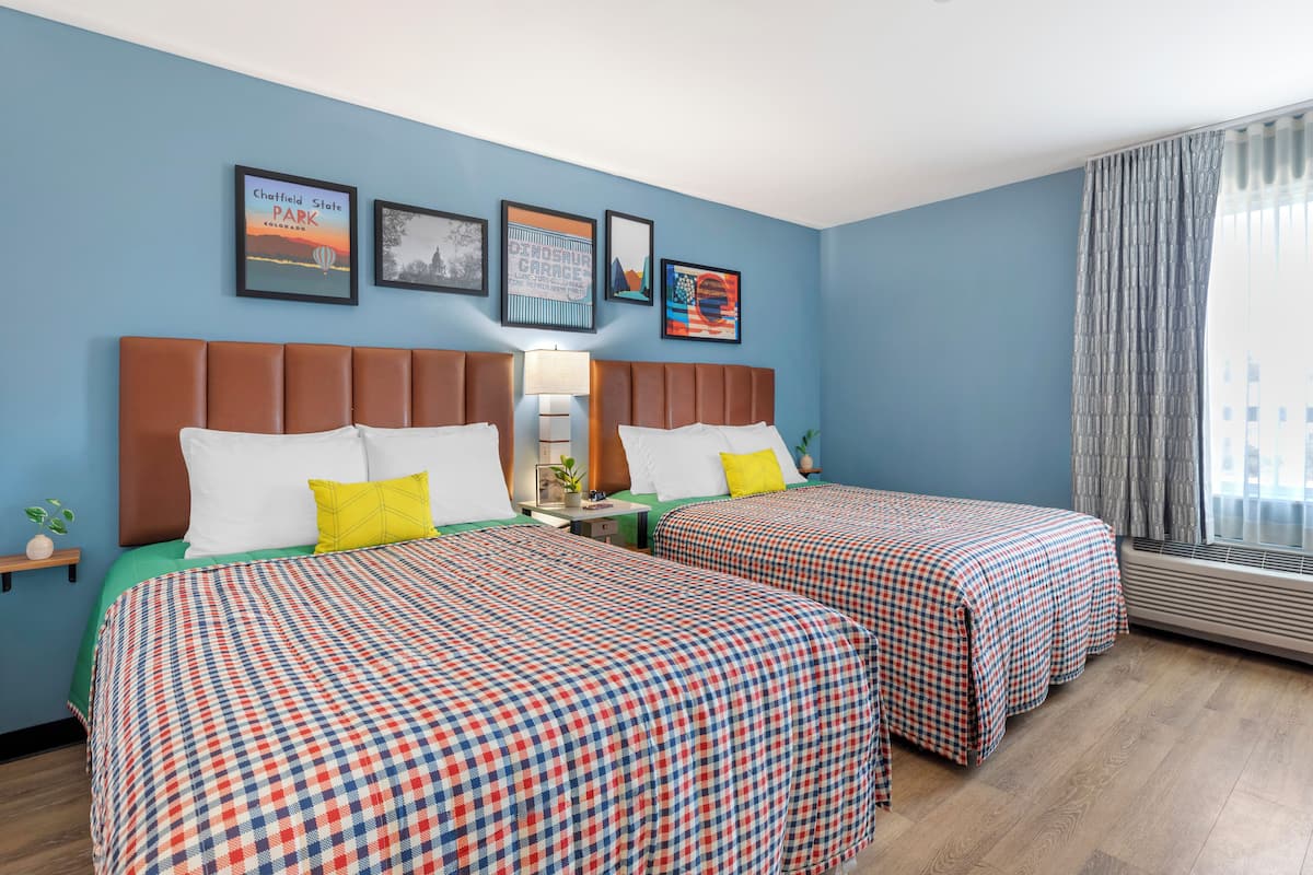 A hotel room with two beds, a nightstand, a lamp, and framed pictures on the wall.