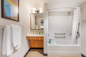 A modern bathroom with a white bathtub, a wooden vanity, and a large mirror. - Uptown Suites Extended Stay Denver CO – Centennial (Centennial)