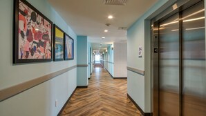 Un pasillo de hotel con piso de madera, paredes azul claro y cuadros en la pared izquierda.