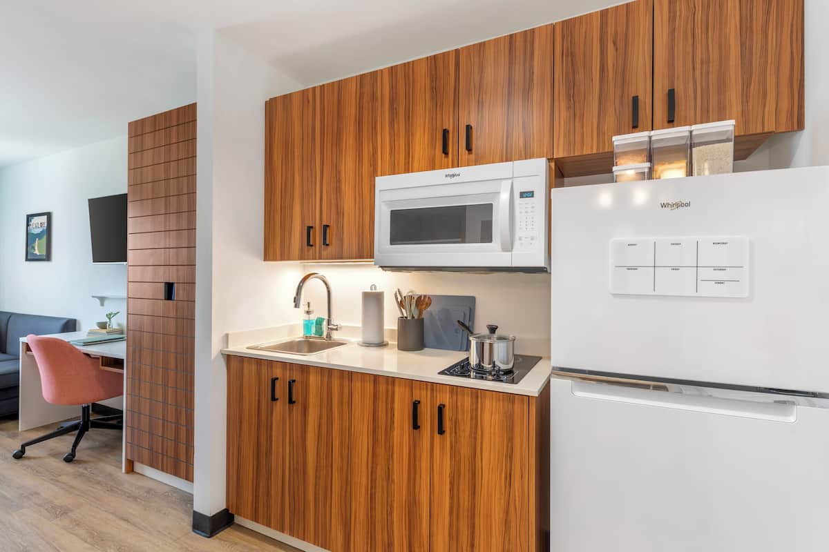 A modern kitchen with wooden cabinets, a microwave, a refrigerator, and a sink.