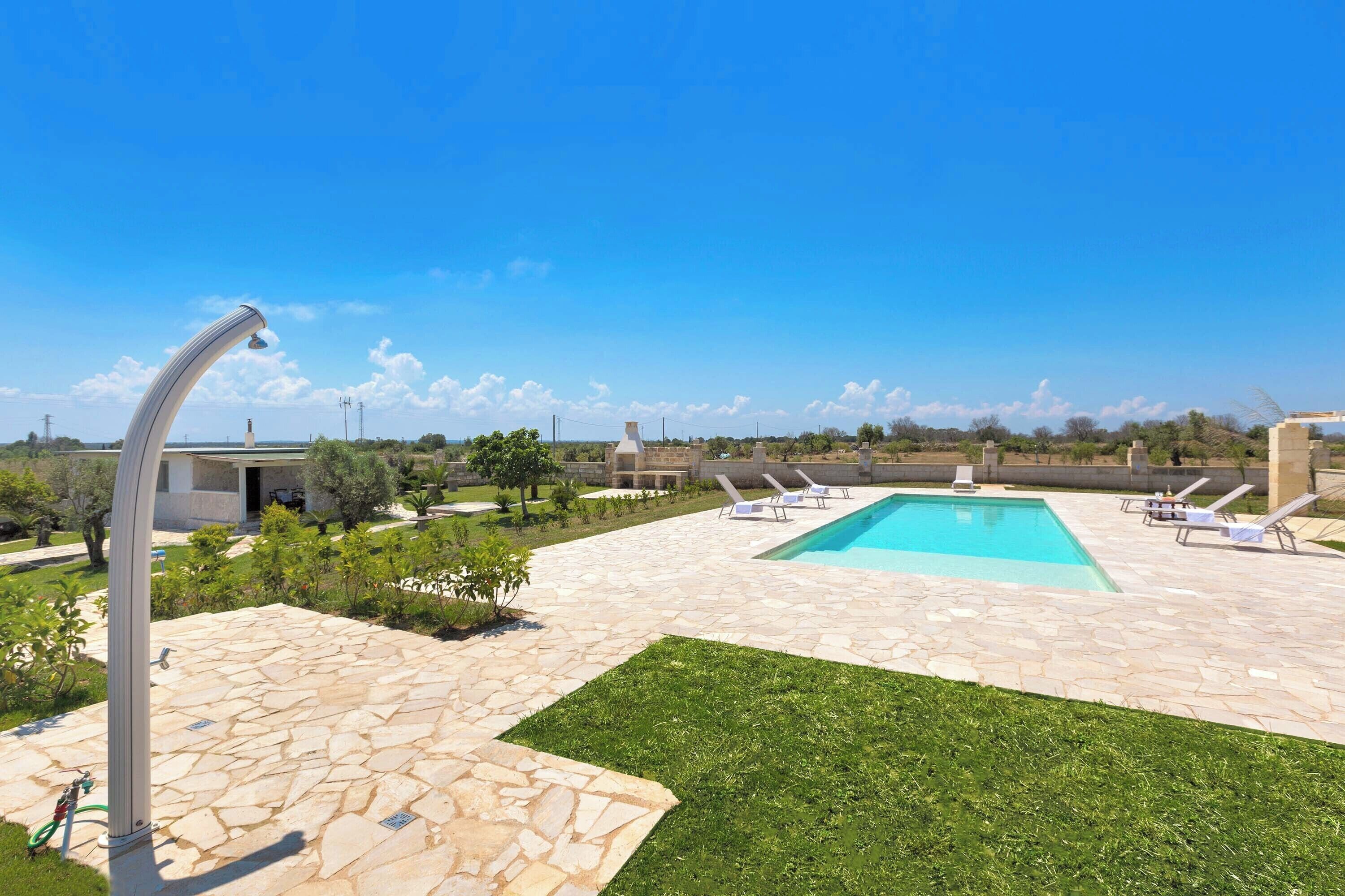 A swimming pool area with stone flooring, a grassy lawn, and lounge chairs.