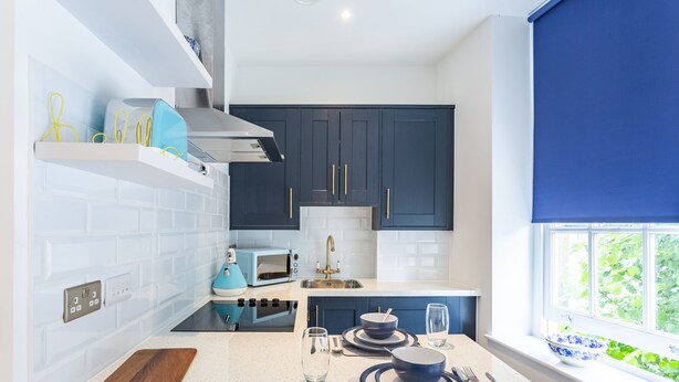 A modern kitchen with white subway tiles, dark blue cabinets, and a window with a view of greenery. - Blue Suede Shoes (Southend-on-Sea)
