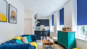 A modern living room with a blue sofa, a wooden coffee table, and a green cabinet. - Blue Suede Shoes (Southend-on-Sea)