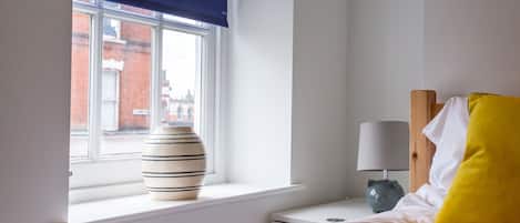 A bedroom with a window, a bedside table with a lamp, and a bed with pillows.