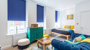 A bedroom with a bed, a blue sofa, a wooden table, and a green cabinet. - Blue Suede Shoes (Southend-on-Sea)