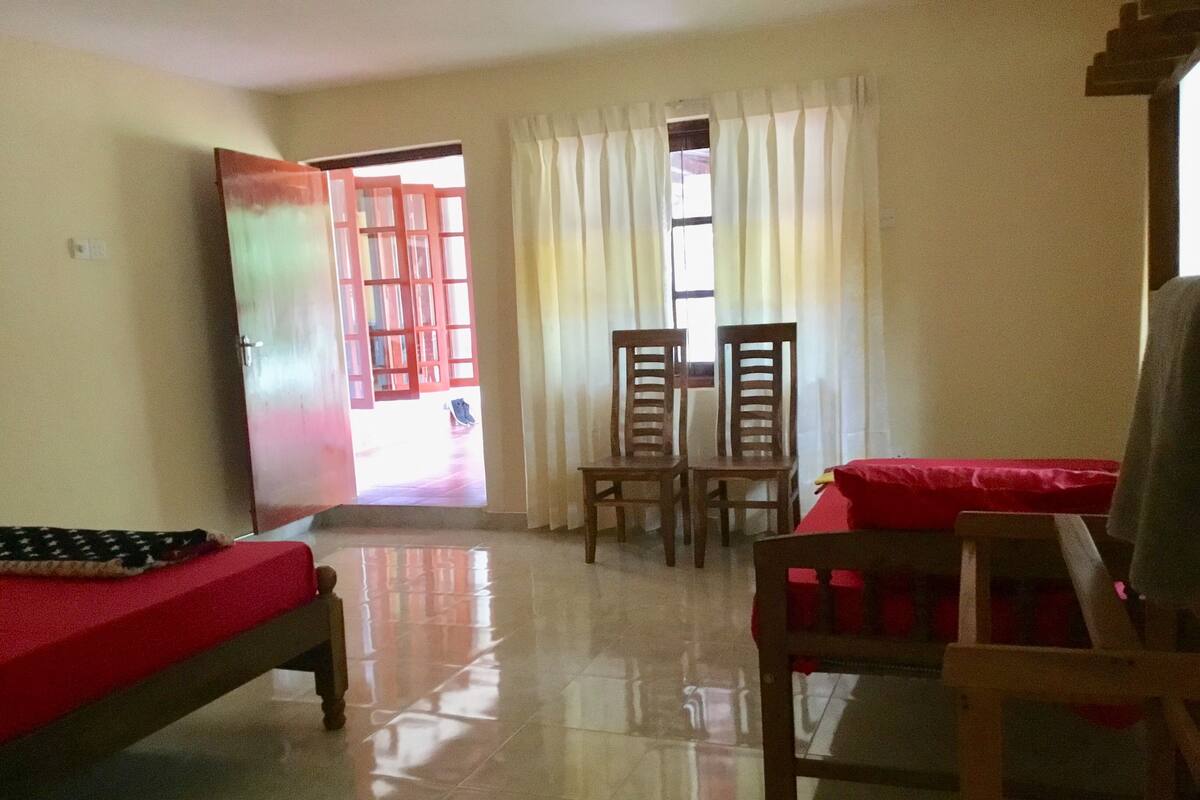Una habitación con cama, una mesa, dos sillas y un ventanal con cortinas.