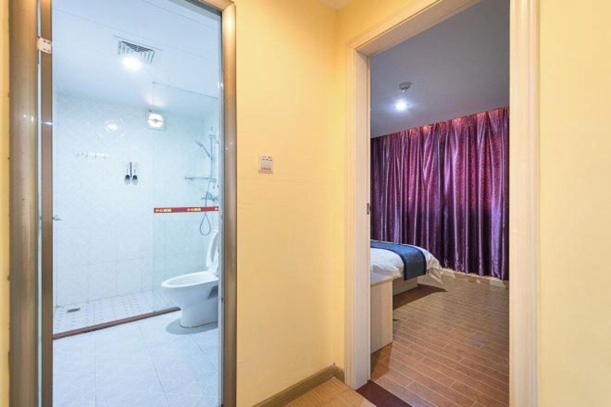 A hotel room with a shower, toilet, and a bed with a curtain.