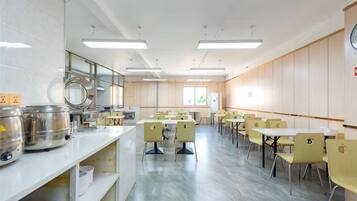 A spacious room with a long table and chairs, a counter with kitchenware, and a clock on the wall.