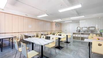 A conference room with tables and chairs, a whiteboard, and a kitchenette area.