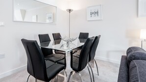 A modern dining area with a glass table surrounded by black chairs, a floor lamp, and framed artwork on the walls.