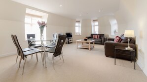 A spacious living area with a glass dining table, modern chairs, a sofa, and a coffee table.
