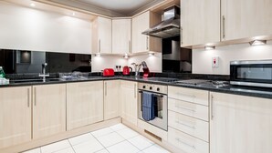 A modern kitchen with light wood cabinets, a stainless steel range hood, a microwave, and a red kettle.