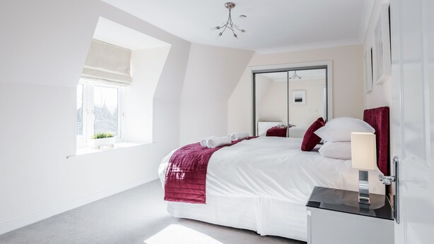 A modern bedroom with a large bed, a bedside table, a window with a view, and a ceiling light.