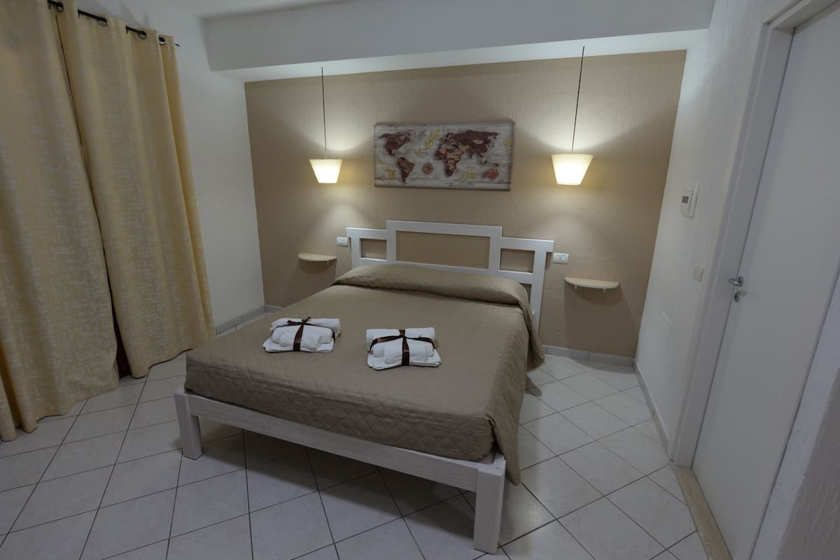 A neatly made bed with two towels, a world map artwork on the wall, and two bedside lamps.