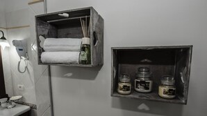 Un baño con un perchero que sostiene dos toallas y un estante con tres frascos de artículos de aseo.