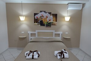 Ein Hotelzimmer mit einem Bett, zwei Nachttischen, einer Wand-Klimaanlage und einem Orchideenbild.