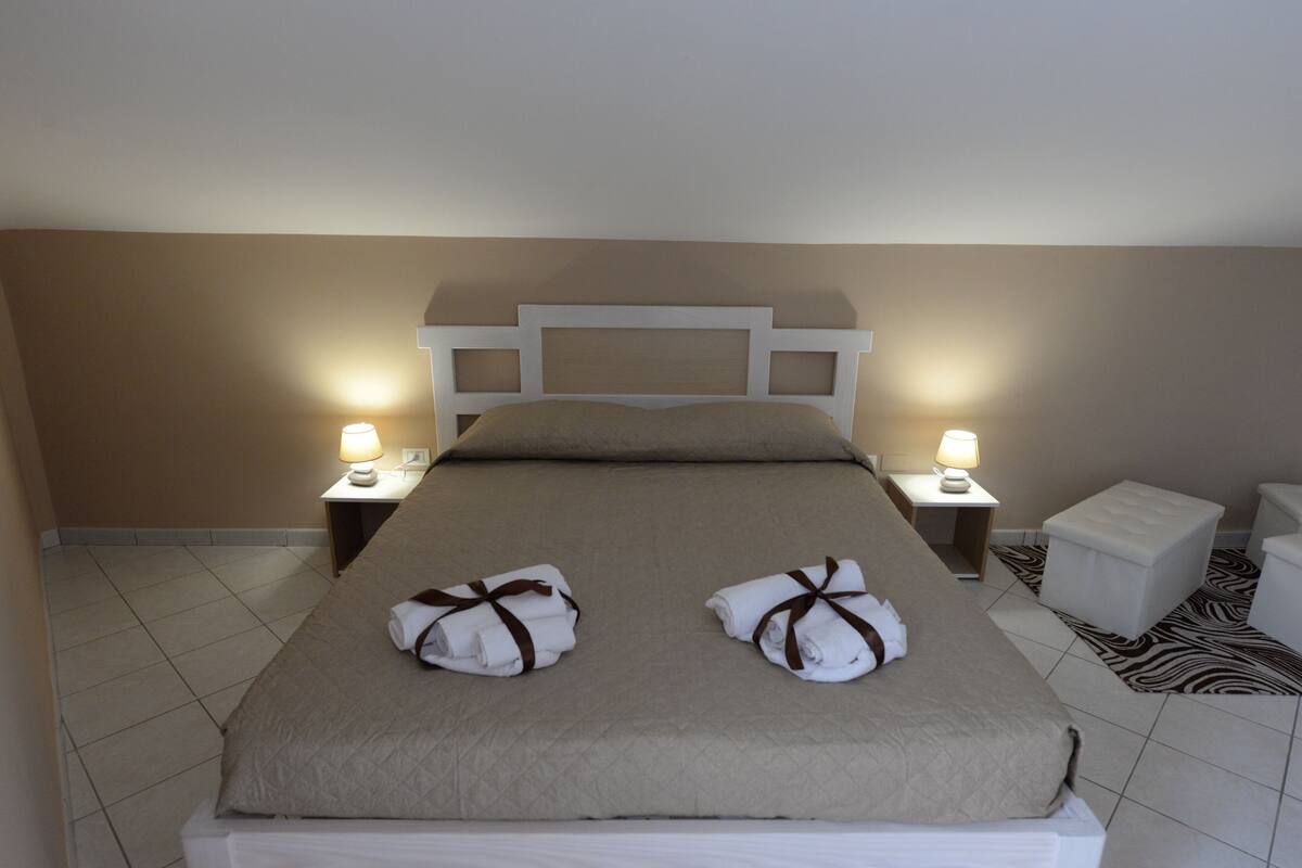 A neatly made bed with two towels, a headboard, bedside lamps, and a zebra-patterned rug.