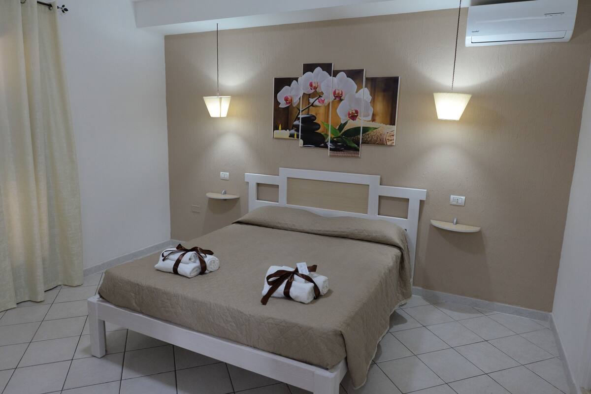 A neatly made bed with towels, a wall-mounted air conditioner, and two wall sconces.
