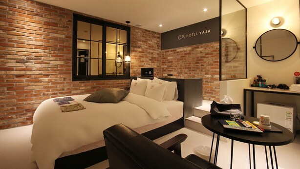 Une chambre d’hôtel moderne avec un mur en briques, un grand lit, un bureau avec une chaise et un miroir rond.