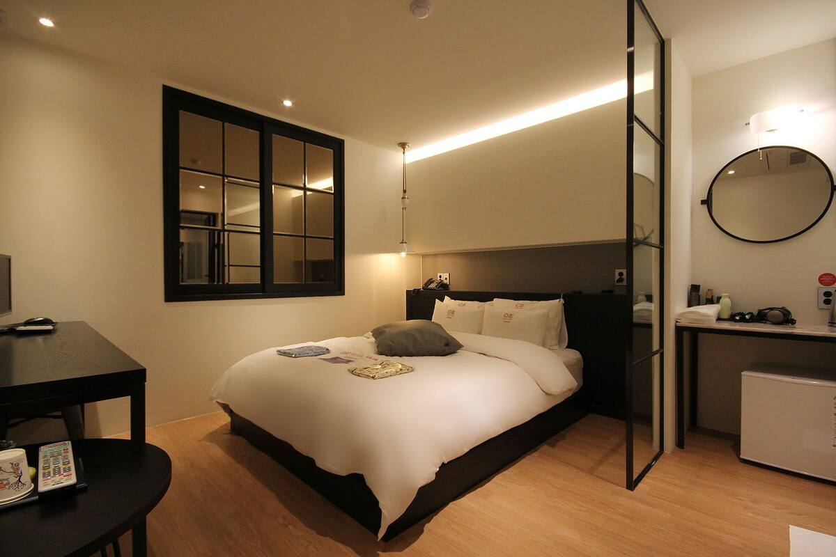 Una habitación de hotel moderna con una cama, una mesita de noche y un escritorio pequeño con una computadora.