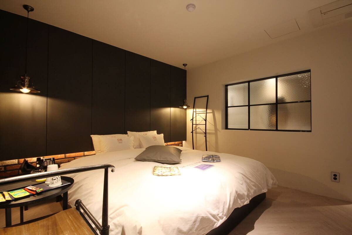 Una cama bien hecha con almohadas, una mesita de noche con lámpara y una ventana con vistas.