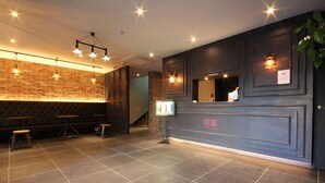 Un hall d’hôtel avec un mur en briques, des lambris en bois foncé et un sol carrelé. On y trouve des tabourets de bar et un comptoir de réception avec une enseigne.