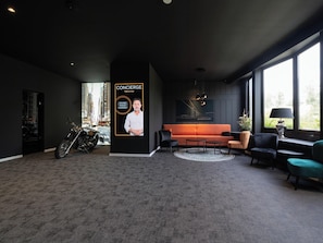 Un salon moderne avec un canapé noir, une moto et une affiche accrochée au mur.