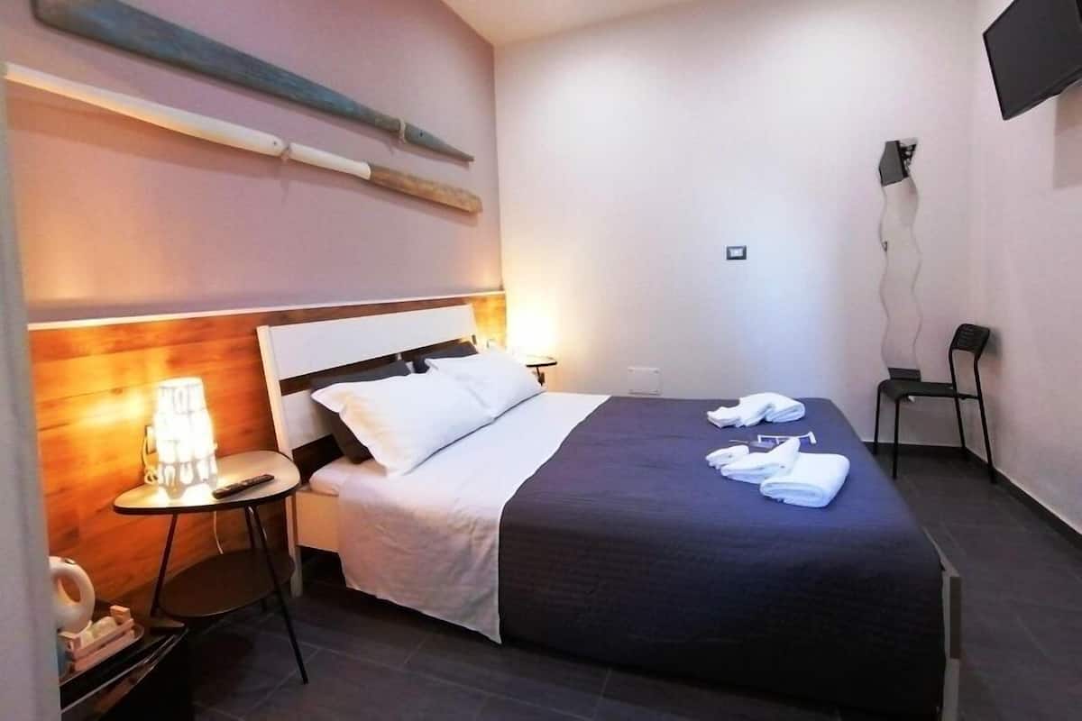 Une chambre d’hôtel avec un lit, une table de chevet avec une lampe, une chaise et un téléviseur fixé au mur.
