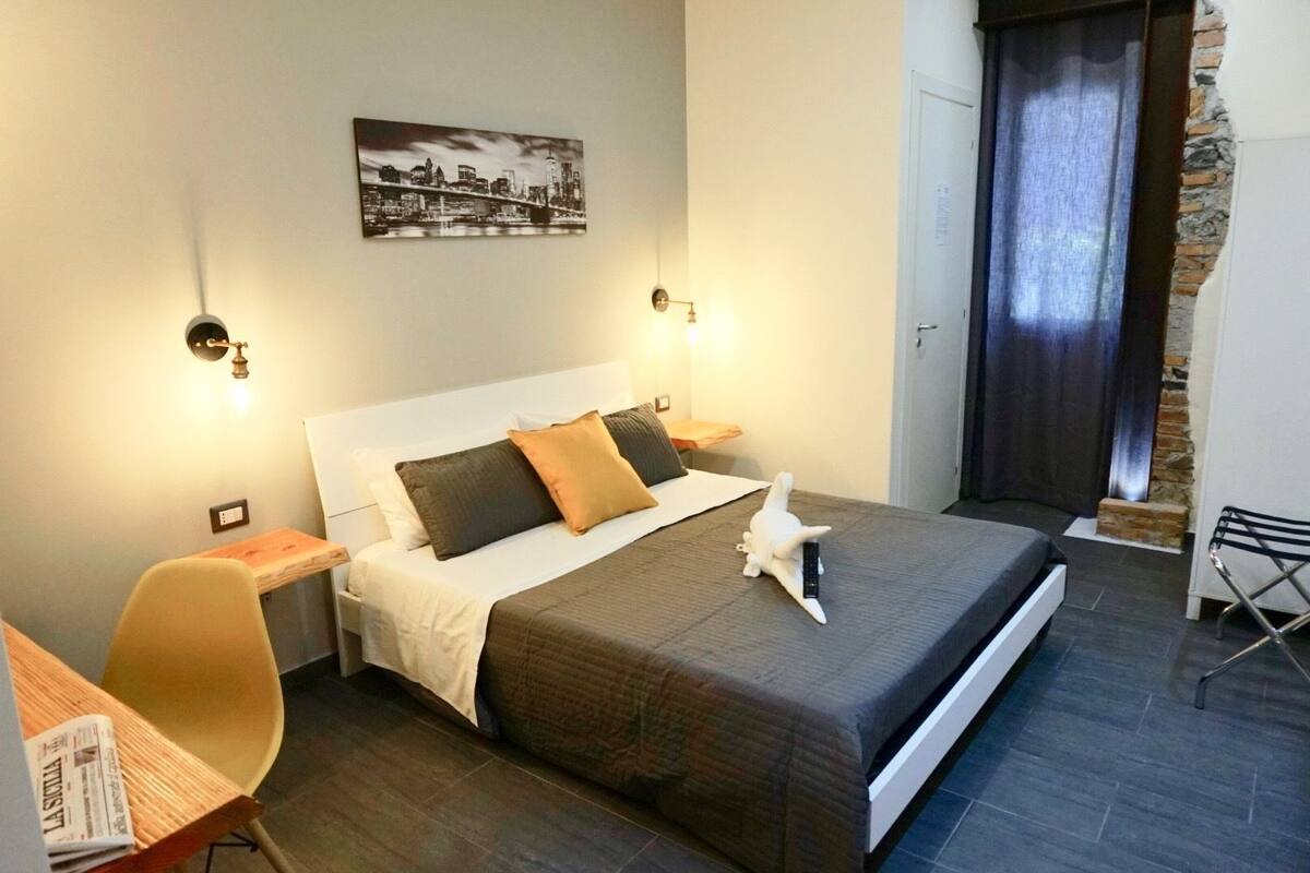 Une chambre d’hôtel moderne avec un grand lit, un bureau, une chaise et un tableau représentant un paysage urbain accroché au mur.