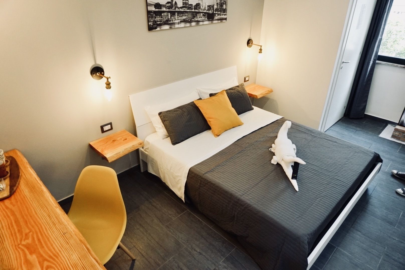 Une chambre d’hôtel comprenant un lit, des tables de chevet, une chaise, un bureau et une œuvre d’art représentant un paysage urbain accrochée au mur.
