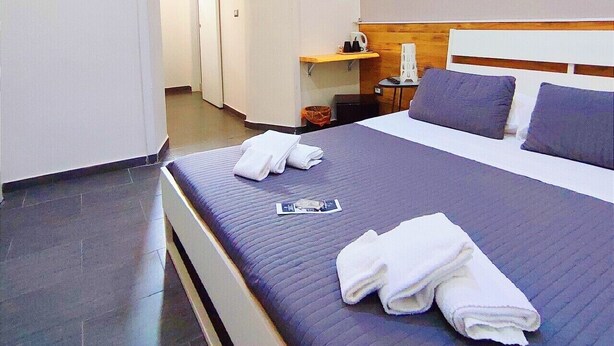 A hotel room with a bed, a nightstand, a wall-mounted shelf, and a door leading to another room. - Passi di Mare Rooms (Giardini Naxos)