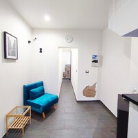 A narrow hallway with a blue sofa, a wooden side table, a clock, and a wall-mounted air conditioner.