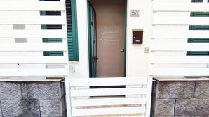 A white building with a stone wall base, a wooden gate, and a door with a welcome sign. - Passi di Mare Rooms (Giardini Naxos)