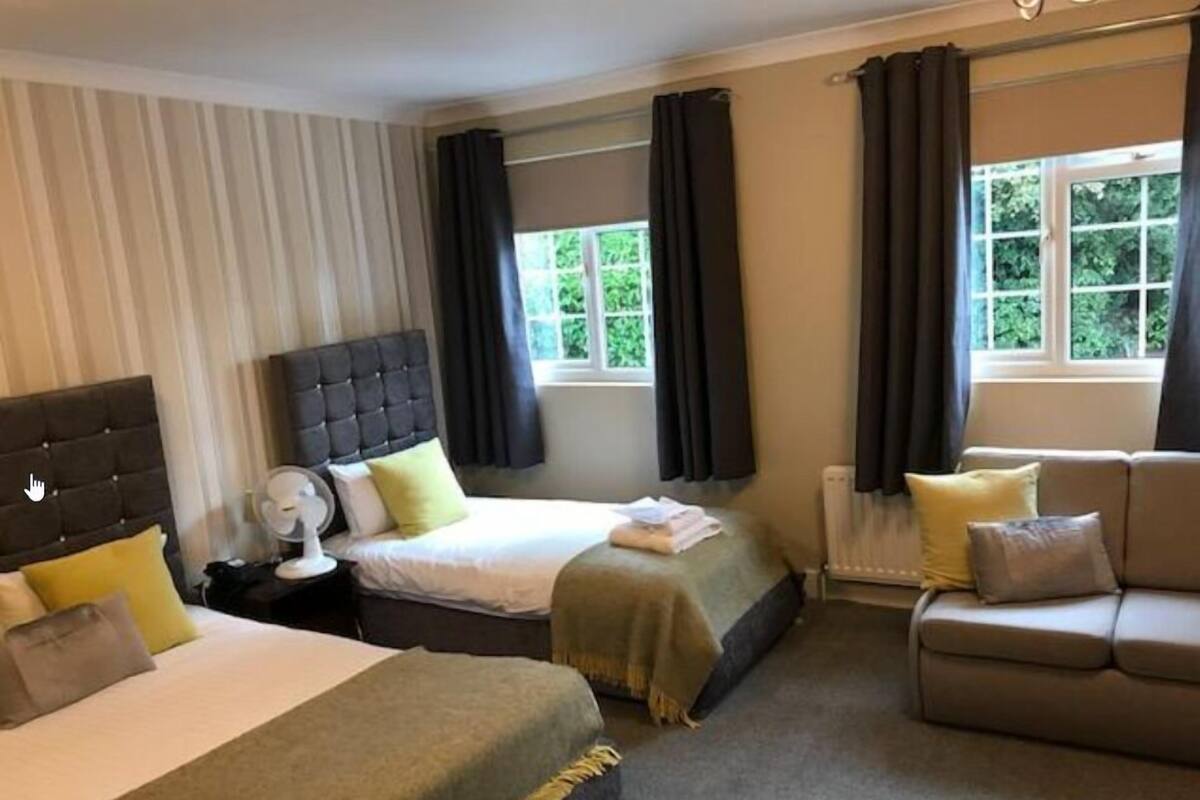 A hotel room with a bed, a sofa, a bedside table with a lamp, and a window with curtains.