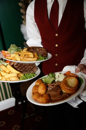 A waiter serving plates of food including steak, fries, peas, and vegetables.