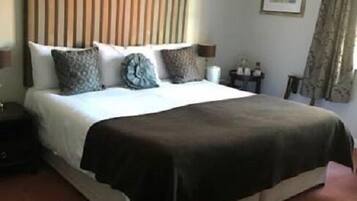 A hotel room with a large bed, a headboard with vertical slats, a bedside table with a lamp, and a framed picture on the wall.