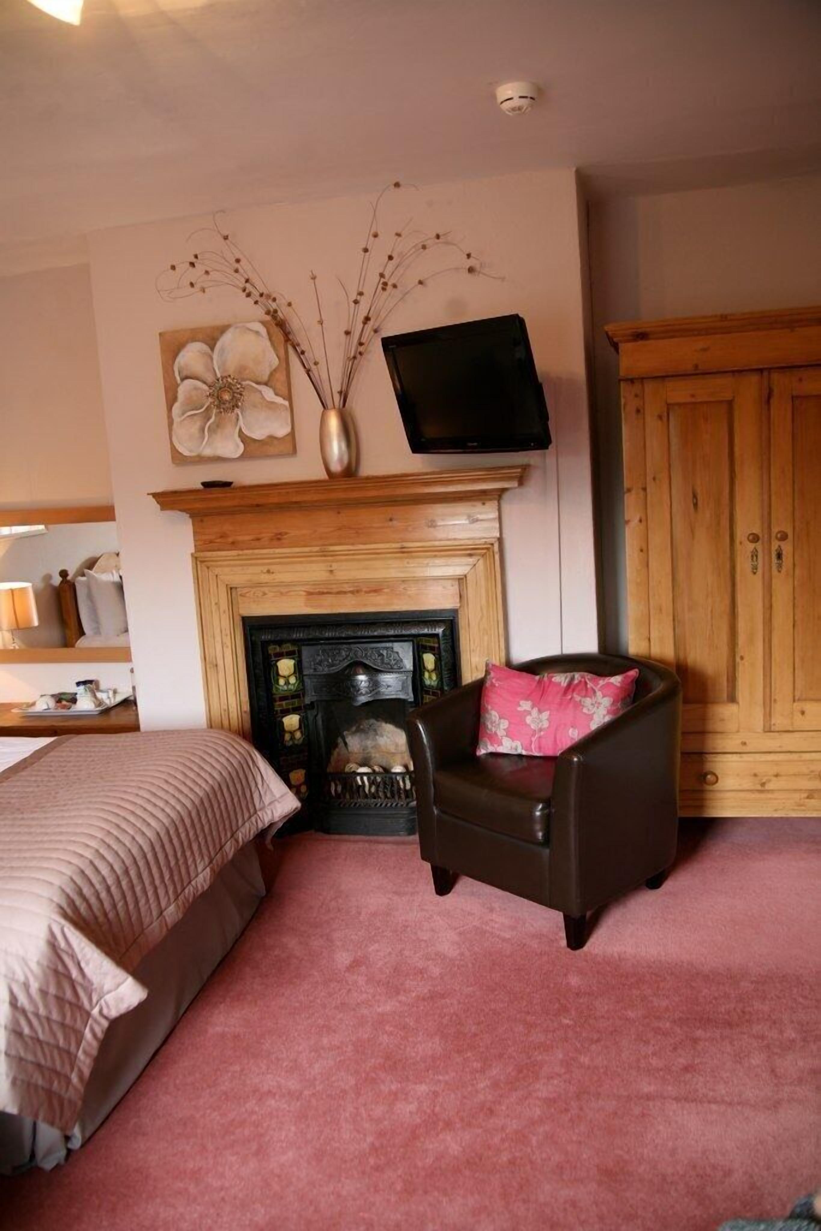 A room with a fireplace, a television mounted above it, a bed with a pink pillow, and a wooden wardrobe.