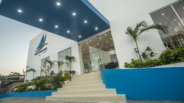 A modern building with a blue and white facade, a staircase leading to the entrance, and palm trees around the base.