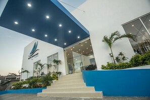 A modern building with a blue and white facade, a staircase leading to the entrance, and palm trees around the base.