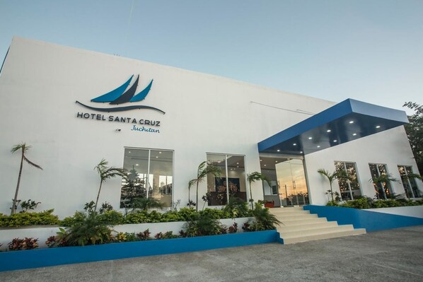 A modern hotel building with a white facade, a blue roof, and a logo featuring a sailboat.