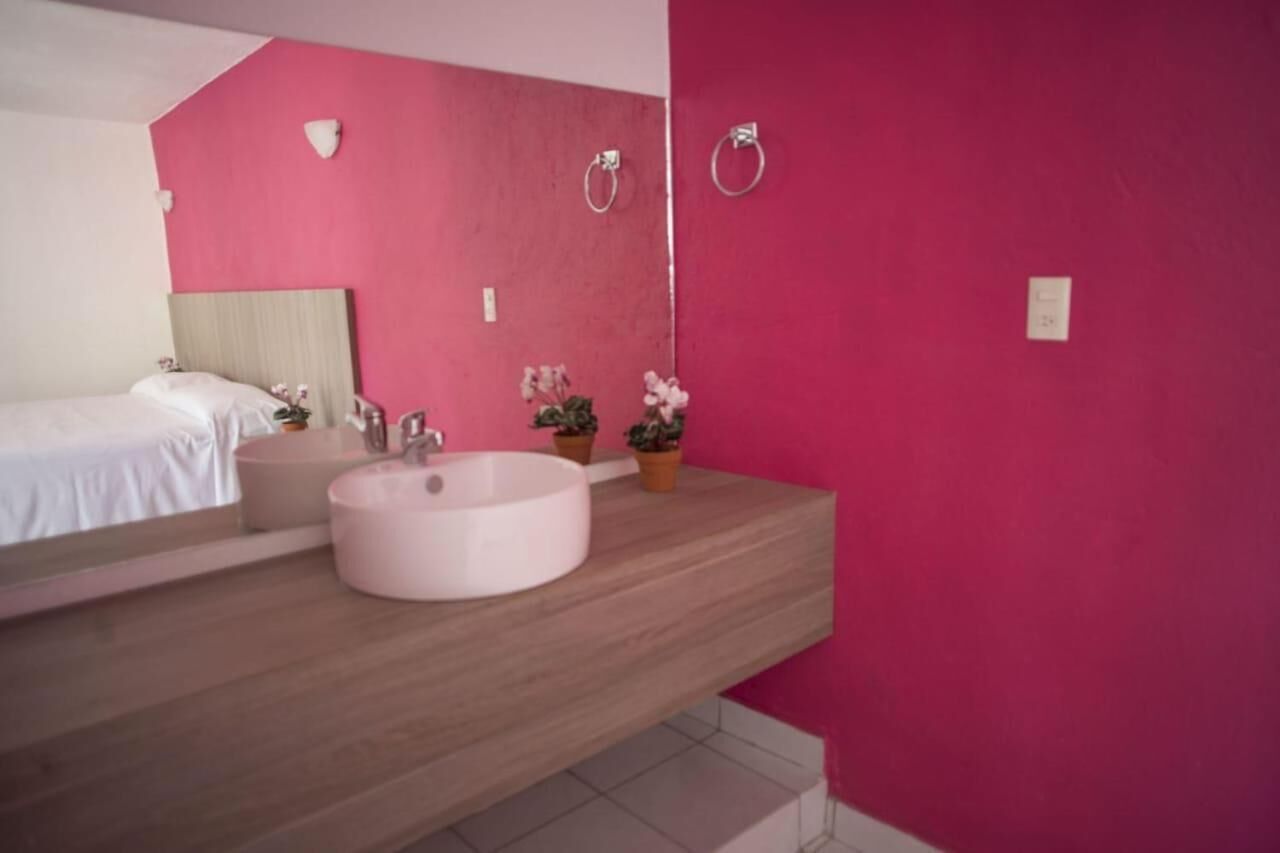 A modern bathroom with a large round sink, a bed, and a pink wall.