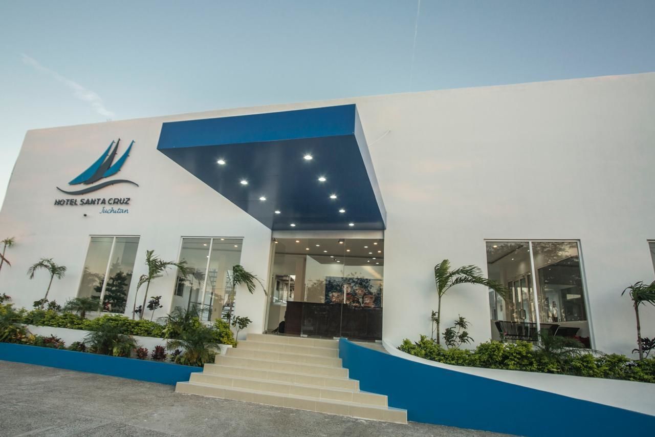 A modern hotel entrance with a blue and white facade, a logo, and a staircase leading to the lobby.