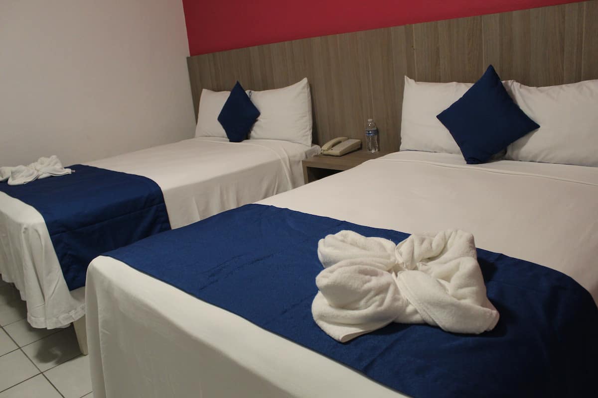 Habitación de hotel con dos camas individuales, cada una con cubrecama azul y ropa de cama blanca. Hay una bata blanca sobre la cama en primer plano.