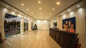 A modern hotel lobby with a reception desk, a Christmas tree, and a large painting on the wall.