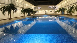 An indoor swimming pool with tiled flooring and palm trees lining the sides.